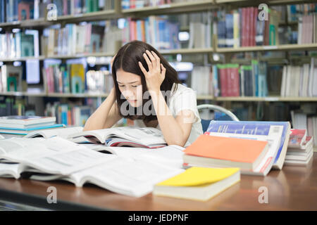 Young Asian student under mental pressure while reading book preparing examination in library at university. Asian student looking stressed. Stock Photo