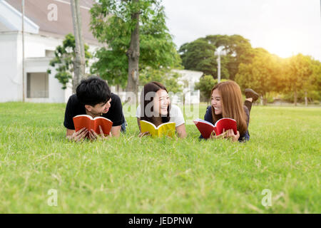 Group of friends studying outdoors in park at school. Three Asian high school student lying in grass at school. Stock Photo