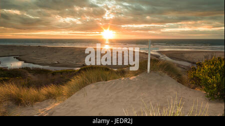 Sun setting at a beach with a white cross on a sand dune. Stock Photo