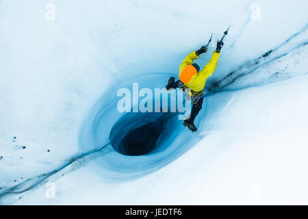 A man lead ice climbing out of a large moulin or hole in the ice of the Matanuska Glacier in Alaska. To start the climb, he and his belayer rappelled  Stock Photo