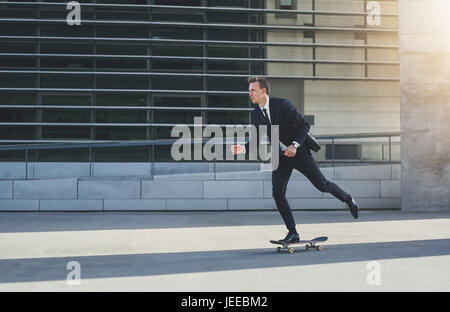 Side view of a businessman in black suit on a skateboard Stock Photo