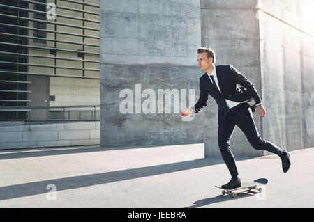 A successful businessman wearing suit riding a skateboard in the street. Stock Photo