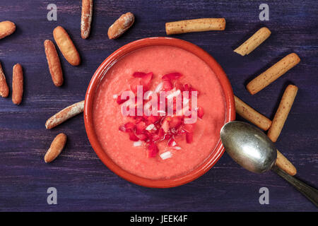 A photo of gazpacho, traditional Spanish cold soup, with bread sticks, shot from above on a deep purple wooden texture with a place for text Stock Photo