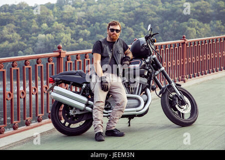 Bearded redhead biker with beard in leather jacket near bike. Stock Photo