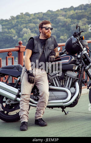 Bearded redhead biker with beard in leather jacket near bike. Stock Photo