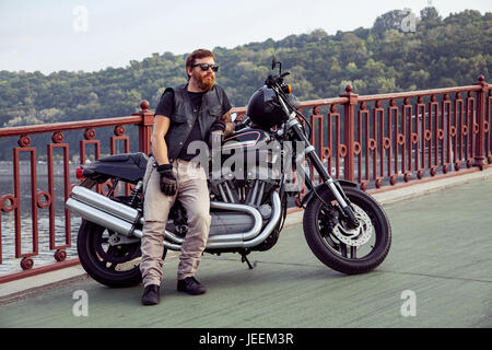 Bearded redhead biker with beard in leather jacket near bike. Stock Photo