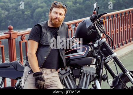 Bearded redhead biker with beard in leather jacket near bike. Stock Photo