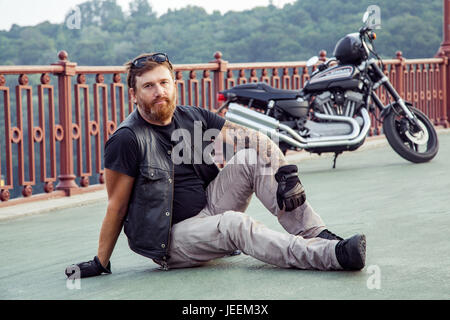 bearded redhead biker with beard in leather jacket sitting on floor. Stock Photo