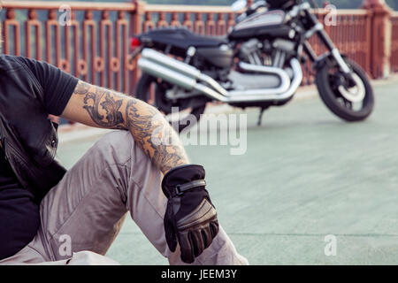 bearded redhead biker with beard in leather jacket sitting on floor. Stock Photo