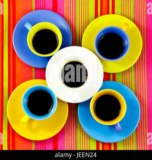 flat lay coffee four color bright cups with different bright plates under them on colored background. One different white cups over all Stock Photo