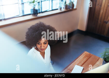 Top view shot of young woman sitting at her desk and working on computer. African female executive working in office. Stock Photo