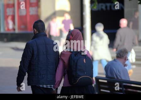 Asian family refugee dressed Hijab scarf on street in the UK everyday scene young couple girl headphones on scarf listening to music Stock Photo