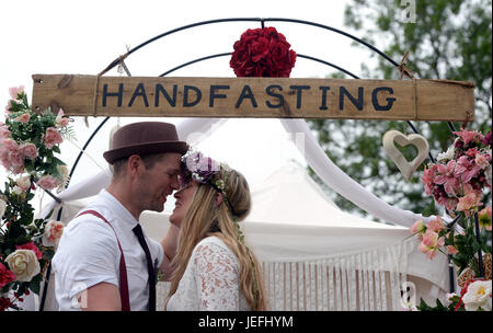 Fi Sexton, 32 and Peter Howe, 38, both from London accompanied by son Thomas Howe, 2 take part in a Handfasting wedding ceremony. The ceremony involved tying their hands together with bonds, Jumping a broom and Eating cake and drinking ale together at Glastonbury Festival, at Worthy Farm in Somerset. Stock Photo