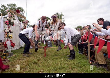 Fi Sexton, 32 and Peter Howe, 38, both from London accompanied by son Thomas Howe, 2 take part in a Handfasting wedding ceremony. The ceremony performed by Glenda proctor (brown) and Jane Tove (green) involved tying their hands together with bonds, Jumping a broom and Eating cake and drinking ale together at Glastonbury Festival, at Worthy Farm in Somerset. Stock Photo