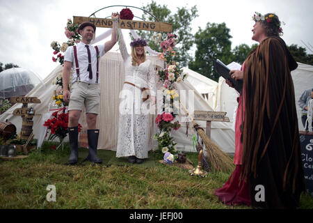 Fi Sexton, 32 and Peter Howe, 38, both from London accompanied by son Thomas Howe, 2 take part in a Handfasting wedding ceremony. The ceremony performed by Glenda proctor (brown) and Jane Tove (green) involved tying their hands together with bonds, Jumping a broom and Eating cake and drinking ale together at Glastonbury Festival, at Worthy Farm in Somerset. Stock Photo