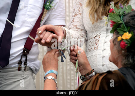 Fi Sexton, 32 and Peter Howe, 38, both from London accompanied by son Thomas Howe, 2 take part in a Handfasting wedding ceremony. The ceremony involved tying their hands together with bonds, Jumping a broom and Eating cake and drinking ale together at Glastonbury Festival, at Worthy Farm in Somerset. Stock Photo