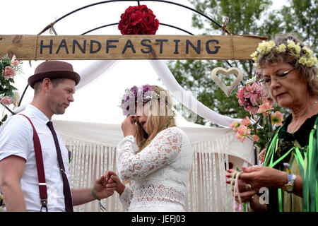 Fi Sexton, 32 and Peter Howe, 38, both from London accompanied by son Thomas Howe, 2 take part in a Handfasting wedding ceremony. The ceremony involved tying their hands together with bonds, Jumping a broom and Eating cake and drinking ale together at Glastonbury Festival, at Worthy Farm in Somerset. Stock Photo