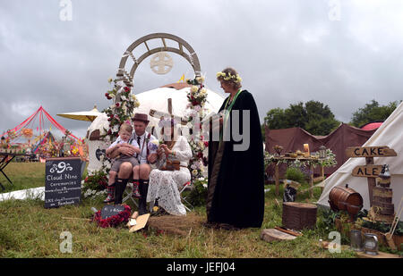 Fi Sexton, 32 and Peter Howe, 38, both from London accompanied by son Thomas Howe, 2 take part in a Handfasting wedding ceremony. The ceremony involved tying their hands together with bonds, Jumping a broom and Eating cake and drinking ale together at Glastonbury Festival, at Worthy Farm in Somerset. Stock Photo