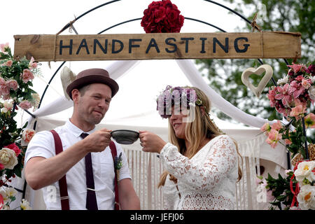 Fi Sexton, 32 and Peter Howe, 38, both from London accompanied by son Thomas Howe, 2 take part in a Handfasting wedding ceremony. The ceremony involved tying their hands together with bonds, Jumping a broom and Eating cake and drinking ale together at Glastonbury Festival, at Worthy Farm in Somerset. Stock Photo