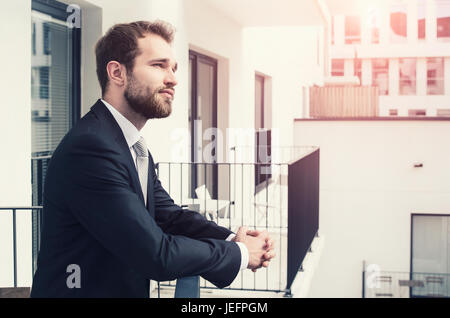 Handsome businessman enjoying view of the city from a balcony. businessman apartment handsome city style people caucasian balcony concept Stock Photo