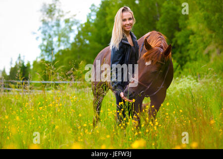 Smiling woman feeding her arabian horse with snacks in the field Stock Photo