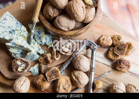 Blue veined stilton served on a wooden board with fresh walnuts in the shell and dried figs. View from above Stock Photo