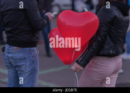 Romantic meeting of guy and girl. Two LED balloons in form of scarlet burning hearts in evening in girl's hand.Romantic background. Concept of love, Valentine's Day Stock Photo