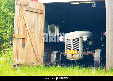 Old grey tractor in a old rustic barn with green background Stock Photo