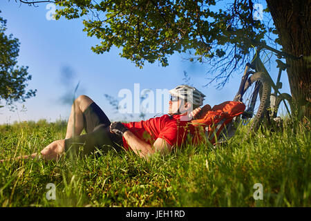 Summer portrait of handsome young man lying on green meadow near bike and backpack. Stock Photo