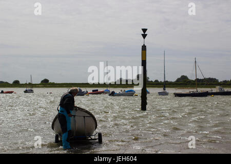 A lone elderly male struggling against high offshore winds to bring his small dinghy ashore to Bosham Harbour slipway in West Sussex, Englandt Stock Photo