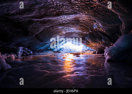 The colors of sunset reflect off the ice inside an ice cave within Augustana Glacier in the Alaska Range in winter; Alaska, United States of America Stock Photo