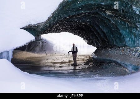 A man on snowshoes stands beneath the ice of Canwell Glacier in the Alaska Range in winter; Alaska, United States of America Stock Photo