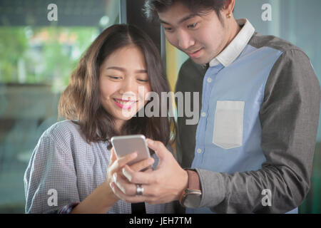asian younger man and woman looking to smart phone screen toothy smiling face happiness emotion Stock Photo