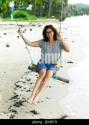 A woman sits on a tree swing on the beach along the Gulf of Thailand; Ko Samui, Chang Wat Surat Thani, Thailand Stock Photo