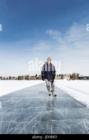 Man skating on freshly groomed ice on lake with houses in the background and blue sky; Calgary, Alberta, Canada Stock Photo