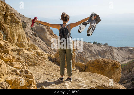 A young woman stands with arms outstretched at the view of the Dead Sea while hiking in Ein Gedi, Dead Sea District; South District, Israel Stock Photo