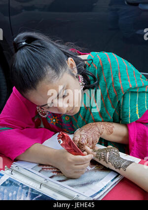 An Islamic woman in traditional clothing decorates a woman's hand with henna to celebrate Eid Al Fitr holiday marking the end on Ramadan. In Queens NY Stock Photo