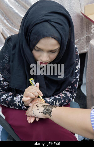 An beautiful Islamic woman in traditional clothing decorates a woman's hand with henna to celebrate Eid Al Fitr holiday marking the end on Ramadan. Stock Photo