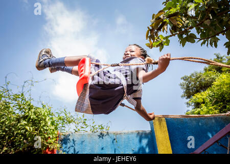 A young girl swinging on a swing in mid-air; Kampala, Uganda Stock Photo