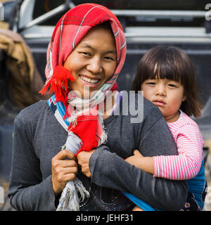 A woman posing with a smile as she carries her young daughter on her back; Tambon Mae Salong Nok, Chang Wat Chiang Rai, Thailand Stock Photo