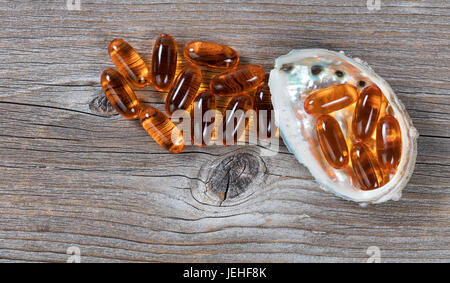 Pacific salmon fish oil capsules and seashell on rustic wood. Flat lay view. Stock Photo