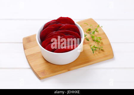 bowl of thin beetroot slices on wooden cutting board Stock Photo