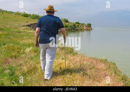 Lonely senior man in blue t-shirt and light pants walking on abrupt riverside of the Dnepr River, Ukraine Stock Photo