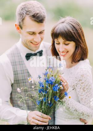 The blue bouqyet of the wild flowers at the blurred background of the newlyweds in the field. Stock Photo