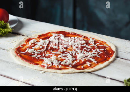 Closeup of a home made raw pizza with cheese and tomato sauce on a wooden background Stock Photo