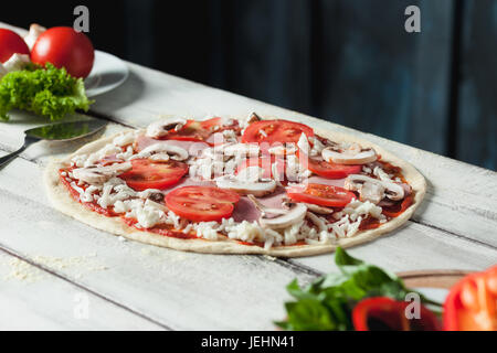 Closeup of a home made raw pizza with cheese and tomato sauce on a wooden background Stock Photo