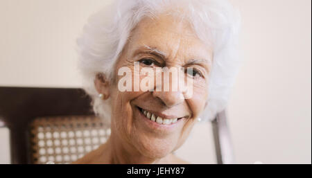 Portrait of old lady sitting on rocker at home. Happy senior woman relaxing on rocking chair and smiling at camera. Stock Photo