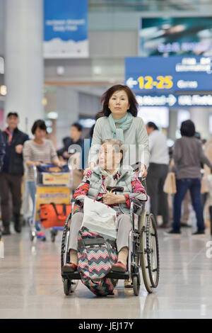 SEOUL-OCT. 24, 2015. Woman with disabled mother in a wheelchair on Incheon International Airport. Since 2005, it has been rated world's best airport. Stock Photo