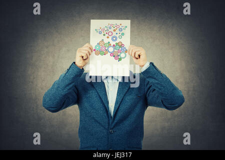 Businessman covering his face using a paper with brain made from gear sketch forming a complet coloruful brain.Finding the righ solution concept. Stock Photo