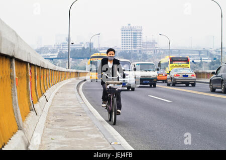 GUANGZHOU-FEB. 21, 2012. Girl on an electric bike with breath protection in a polluted urban environment. Stock Photo